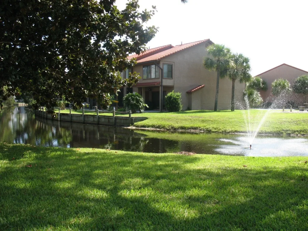 Sun dappled lawn and a pond with a fountain and condos