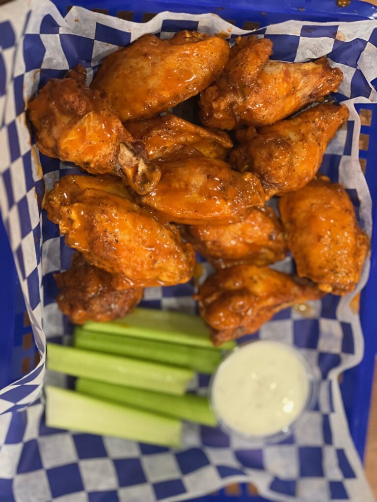 Bone-in Buffalo wings in a blue checkered basket with celery and ranch dressing